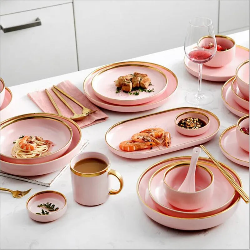 Gilt rim pink porcelain dinner plate from MC The Black Diamonds with matching food dishes and cutlery set on a kitchen table.